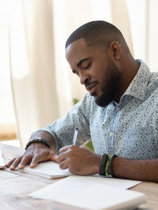 man writing notes at desk