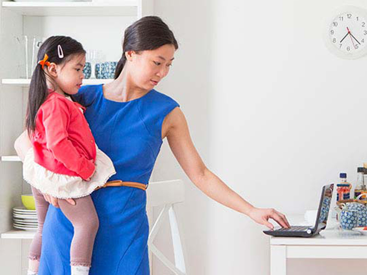 A woman holding a toddler while using one hand to use a laptop
