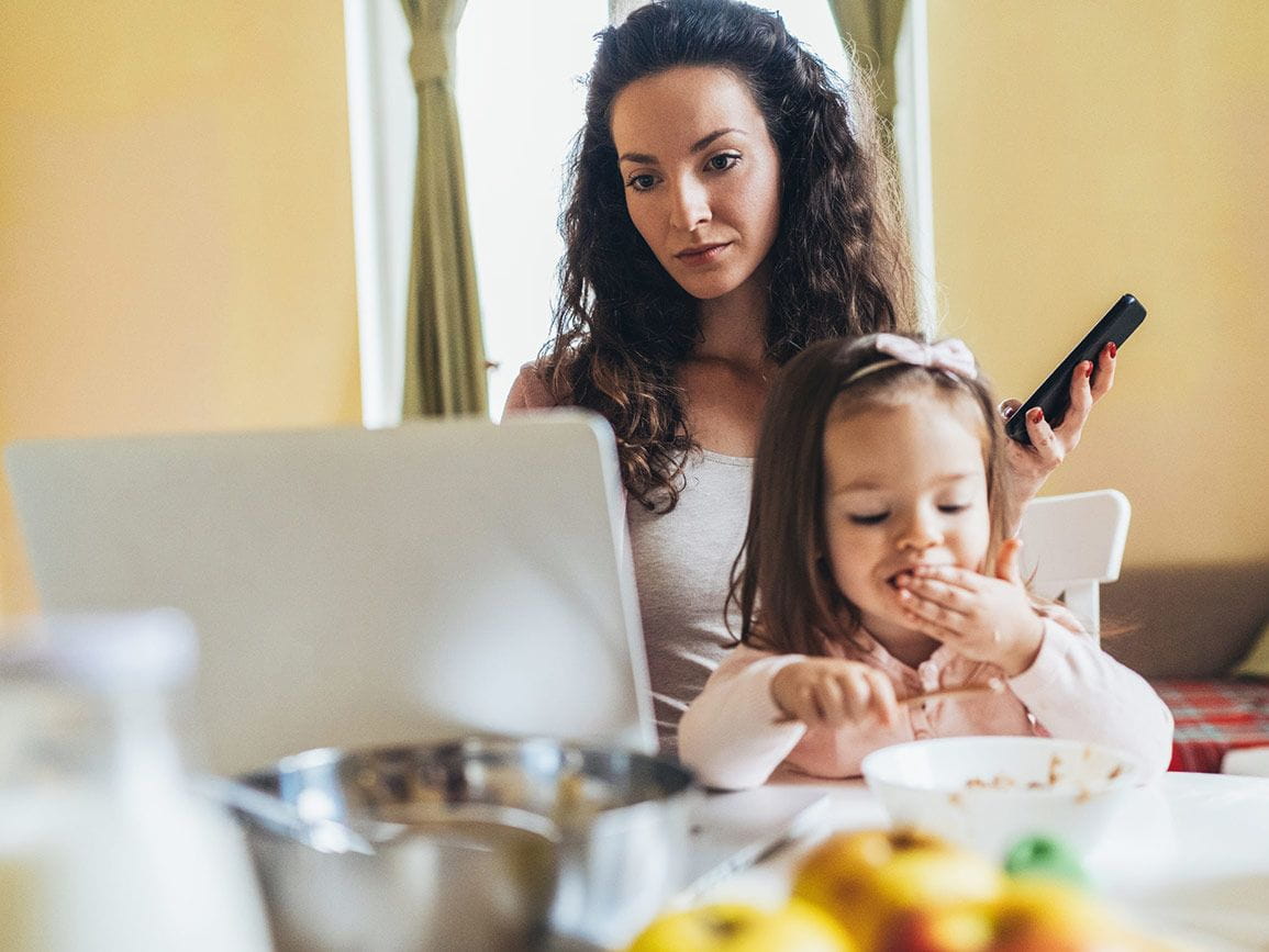 mom working on laptop with daughter eating nearby