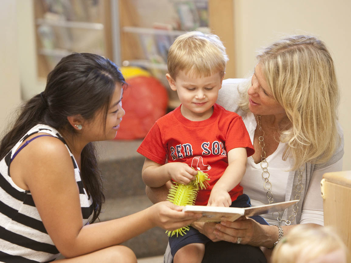 A mother and her son reading a book with their child care teacher