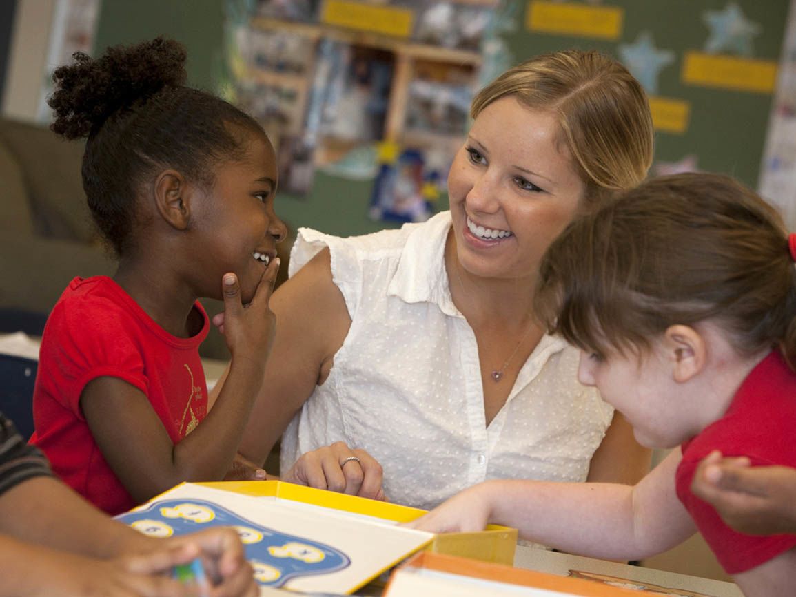 Two toddler girls reading with their child care teacher