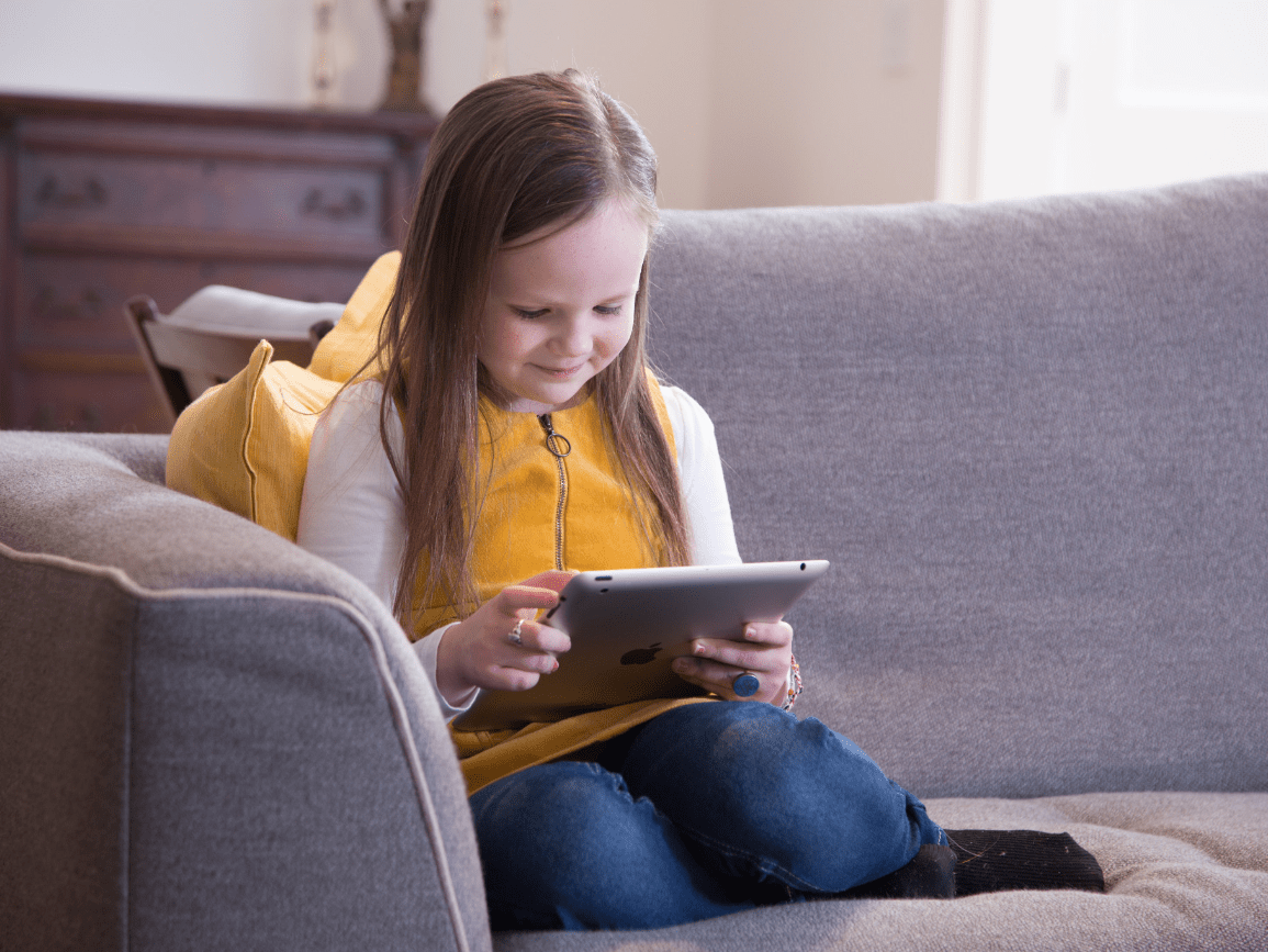 little girl reading tablet on couch