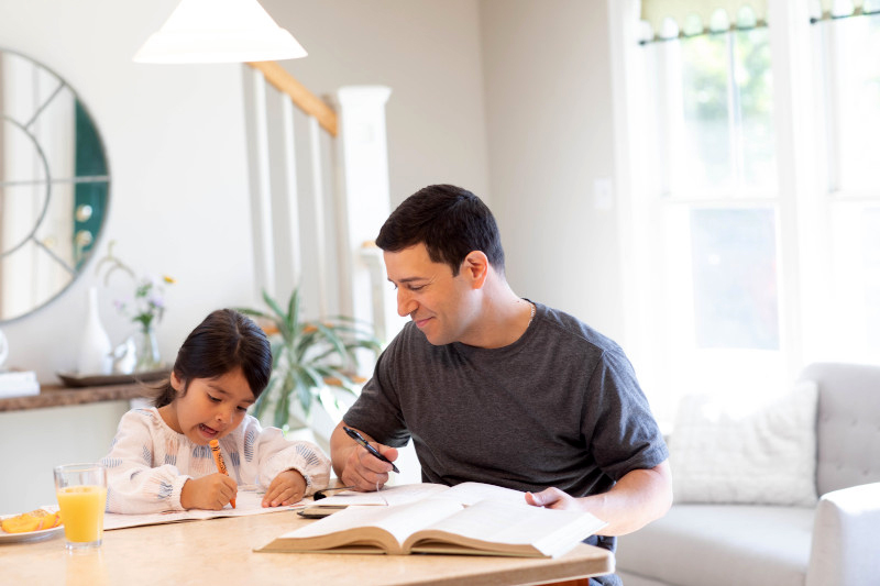 Dad studying and daughter drawing together at home