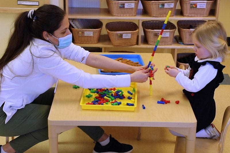 Masked teacher doing a STEM activity with a preschooler