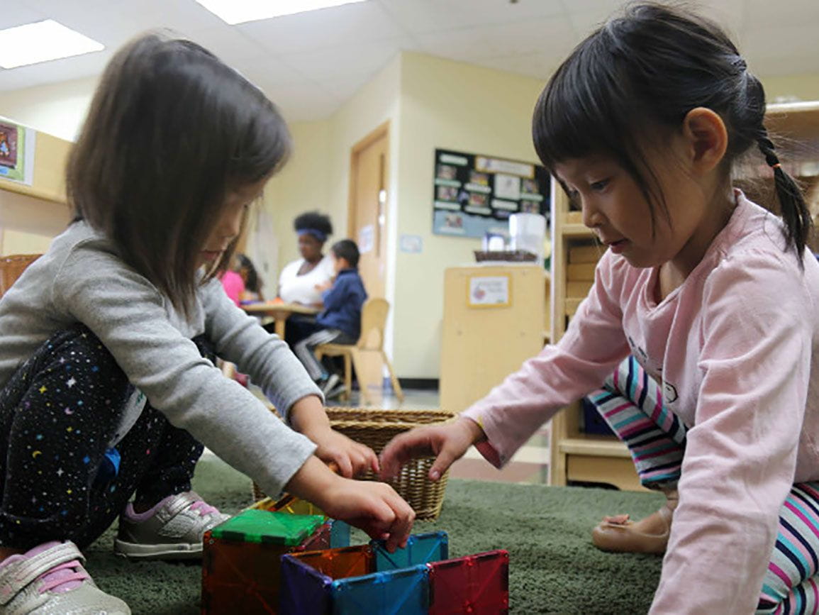 Two preschool girls working together to build a structure