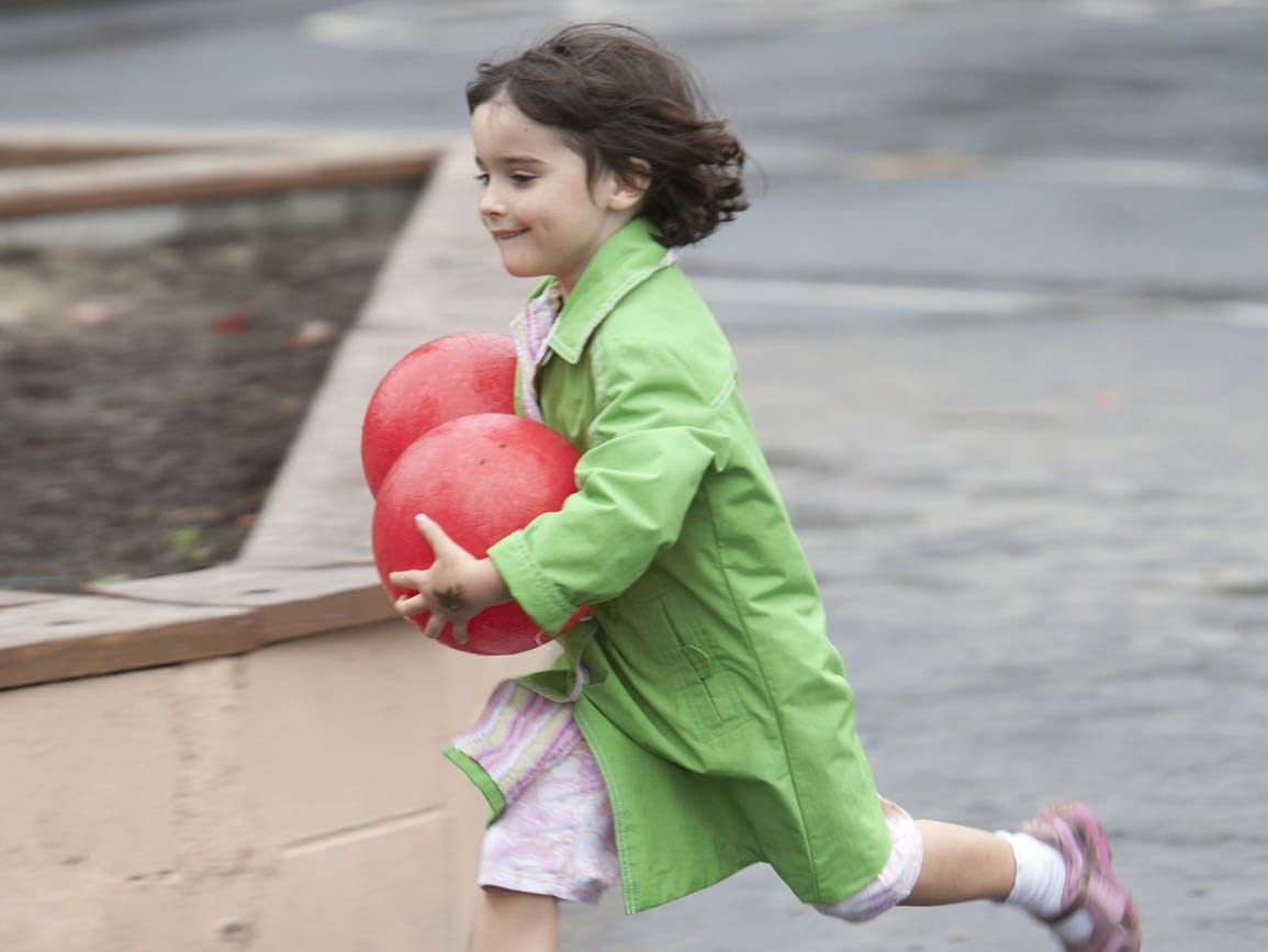 A toddler girl running with two balls