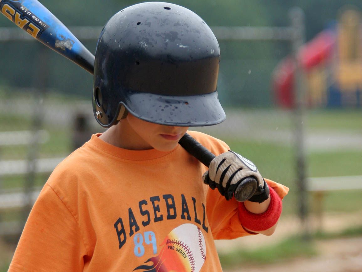 A child in a baseball uniform stepping up to the batter's box