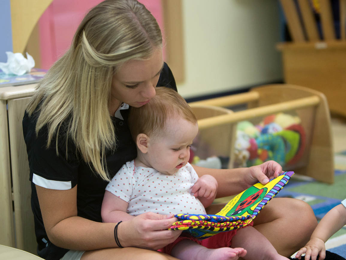 A child care teacher reading to an infant
