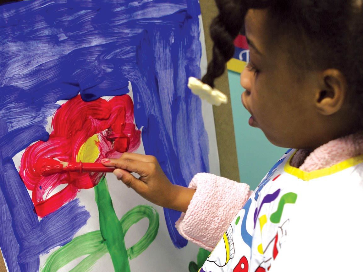 Preschool girl painting a flower at an easel