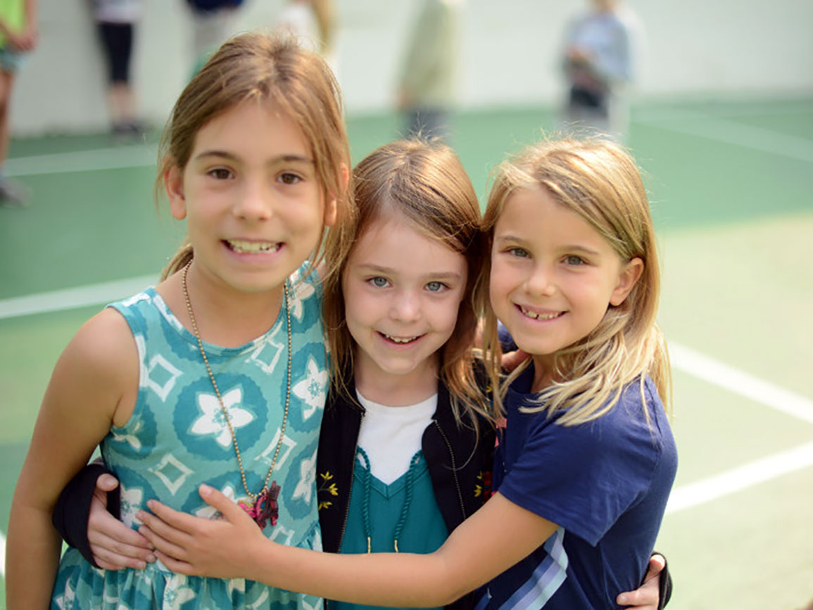 Three school-aged girls arm-in-arm on the playground