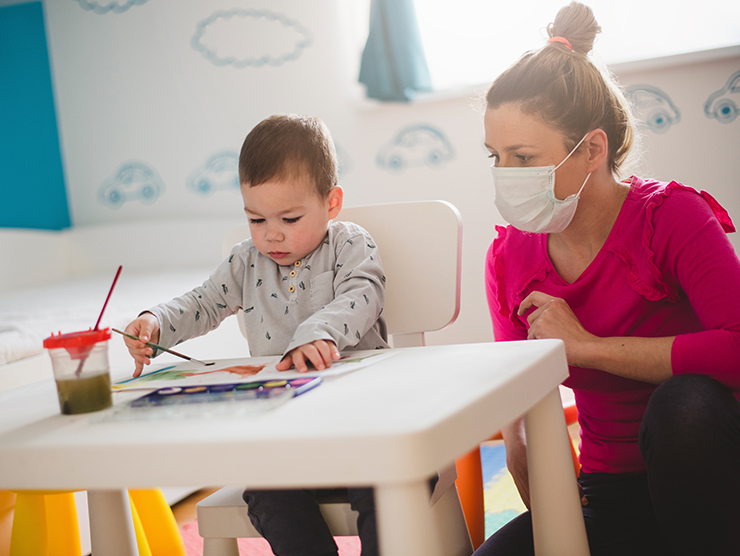 toddler doing an art project with a teacher in a mask