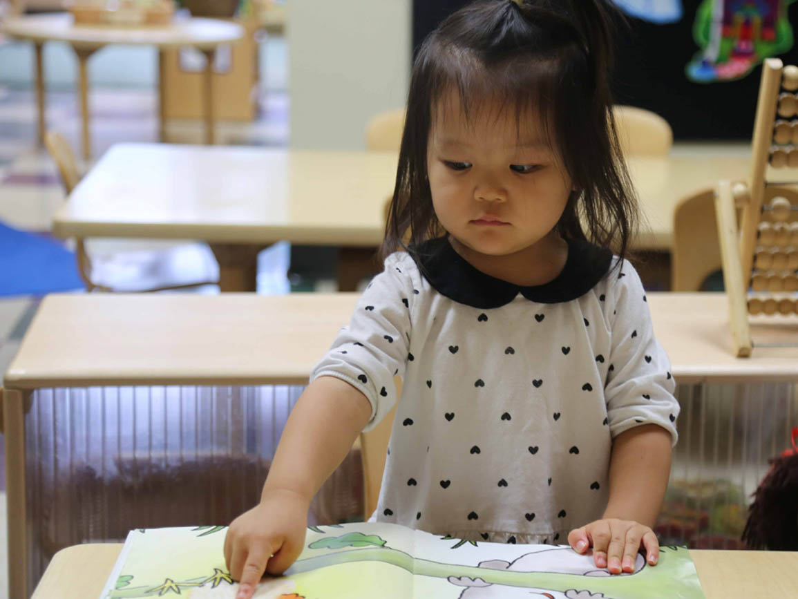 Preschool aged girl pointing to an open book on a desk