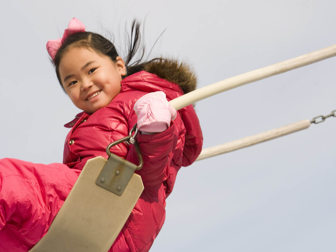 Young girl in a pink coat swinging