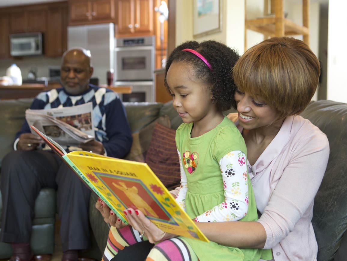 Mom reading to her preschool aged daughter at home on the couch