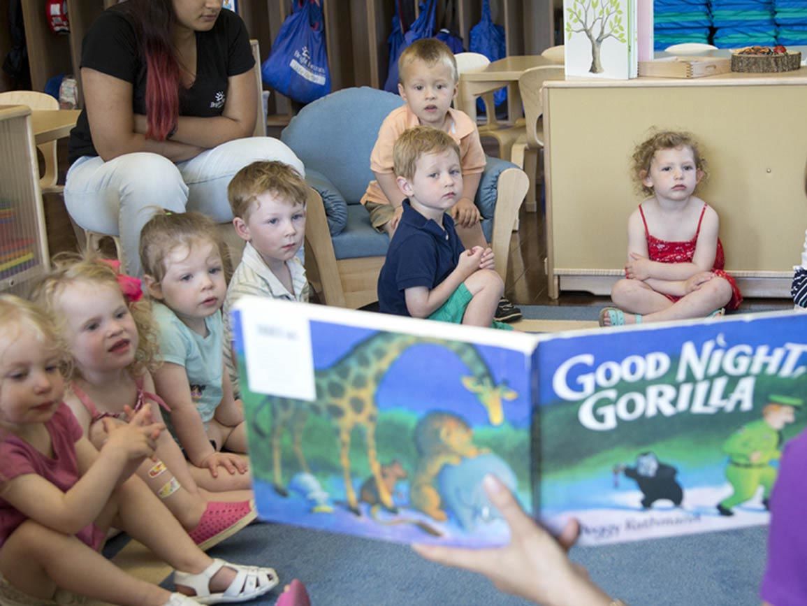 Co-ed group of toddlers sitting & listening to the teacher read aloud