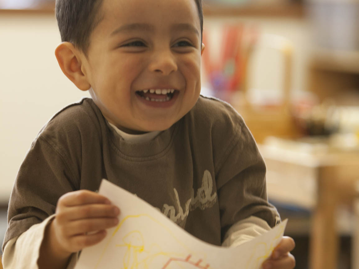 Preschool aged boy smiling and holding his drawing