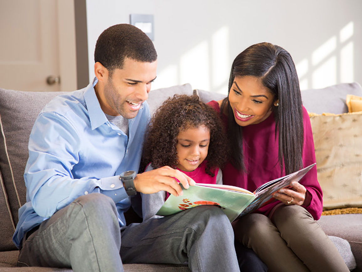 Mom and dad reading with preschool aged daughter on the couch