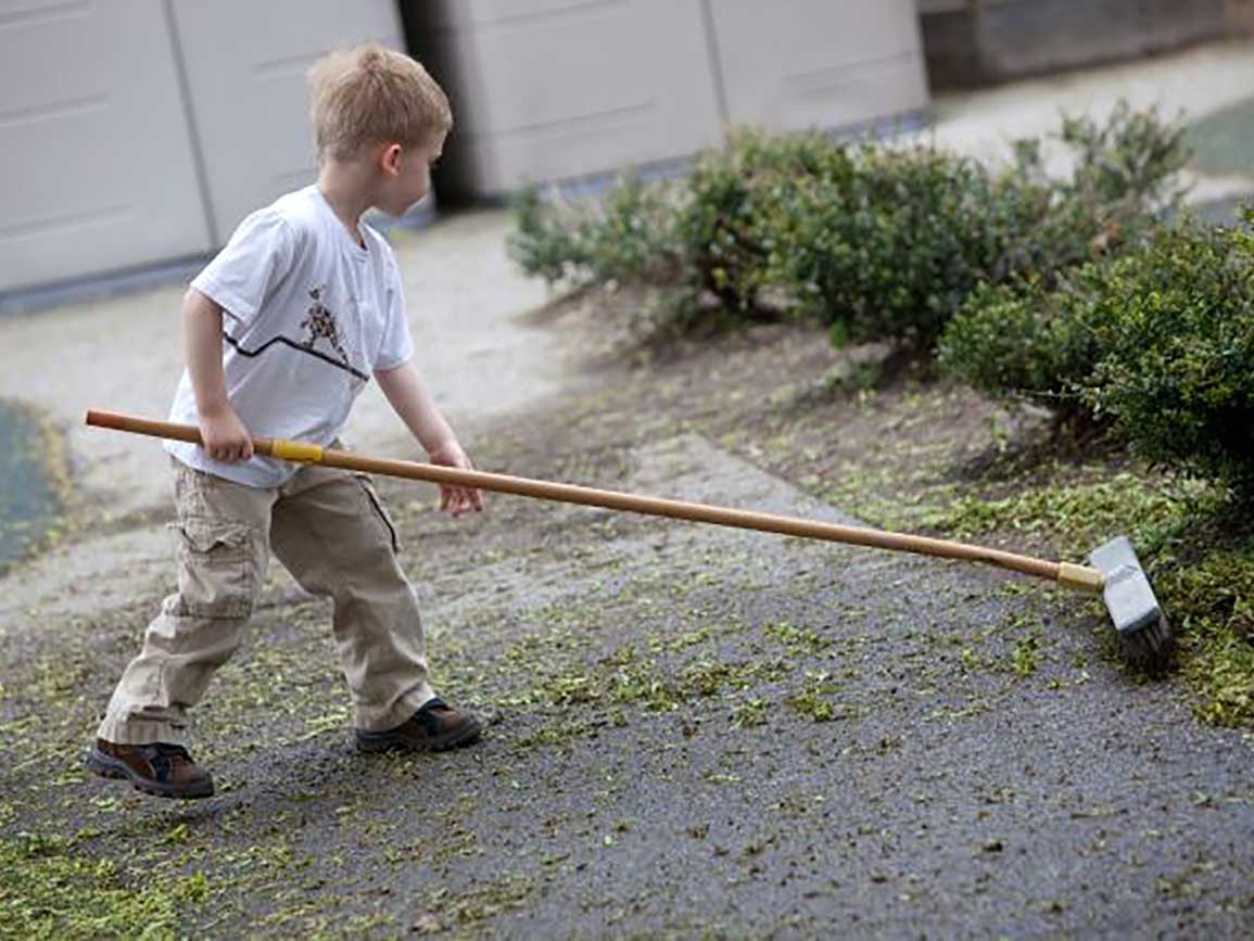 Kindergarten boy sweeping outside