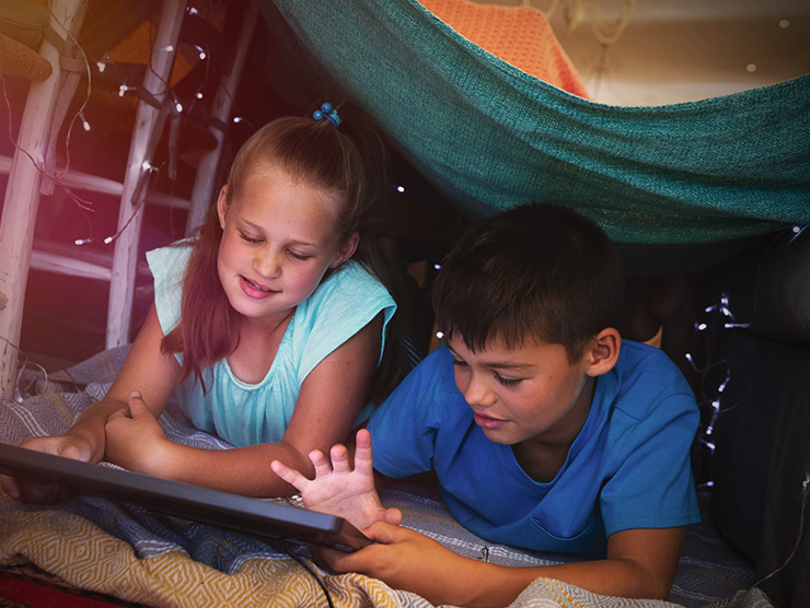 Two school aged kids playing together in a fort at home 