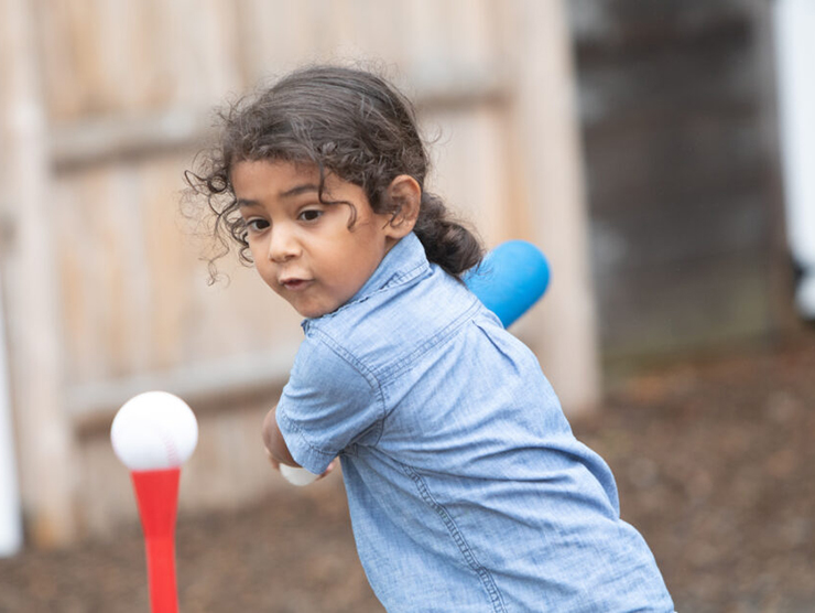 Little girl using a bat to swing at a ball while playing outside 