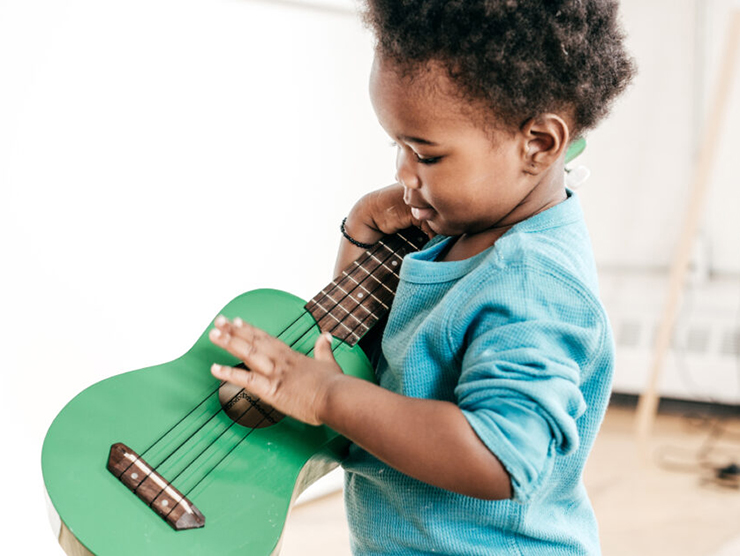 Toddler playing with a guitar to make music at day care 