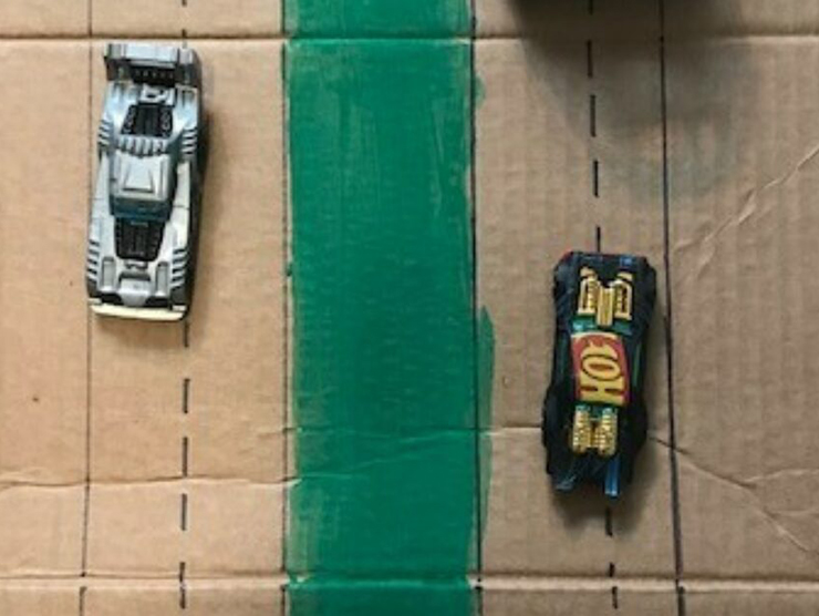 Cardboard with a road drawn on it and toy cars on top