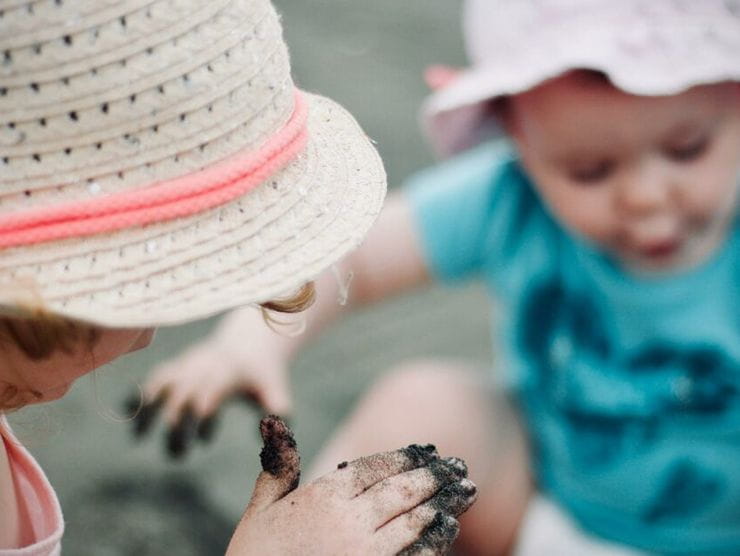 Two toddlers playing with wet sand at the beach 