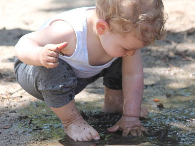 Toddler playing in wet mud outside at day care 