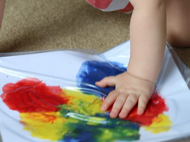 Infants hand in different colored paint on a white tarp 