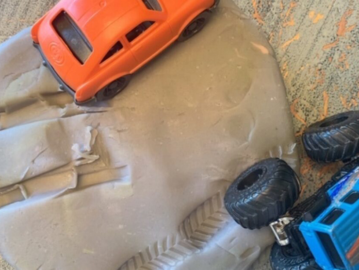 Toy trucks on play dough leaving car tracks 