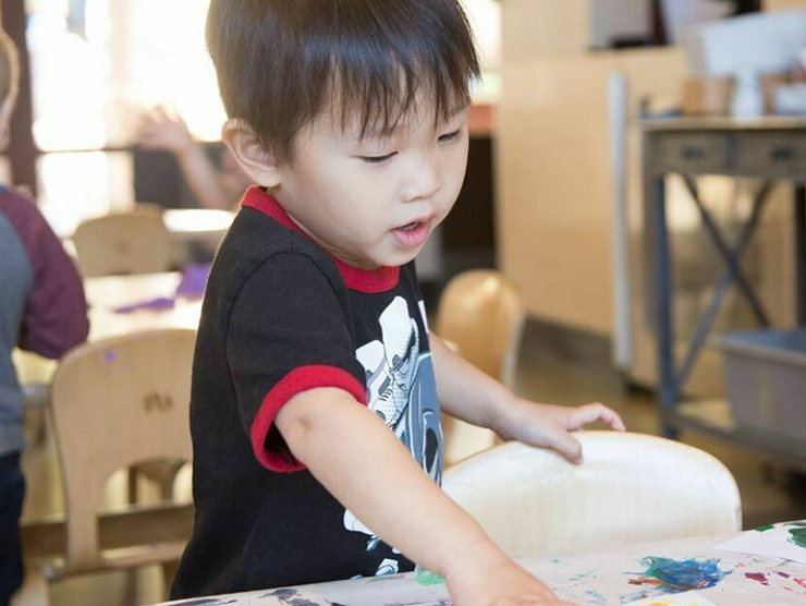 Toddler finger painting with multiple colors on white paper at home 