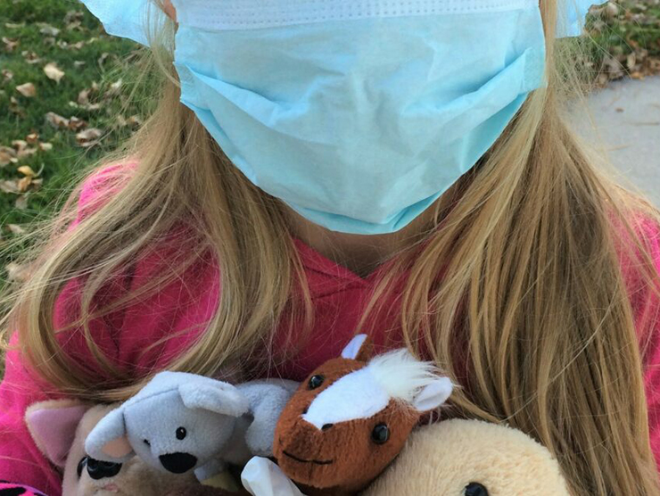 Toddler practicing healthy and safety by wearing a medical mask, cap, and gloves while holding stuffed animals 