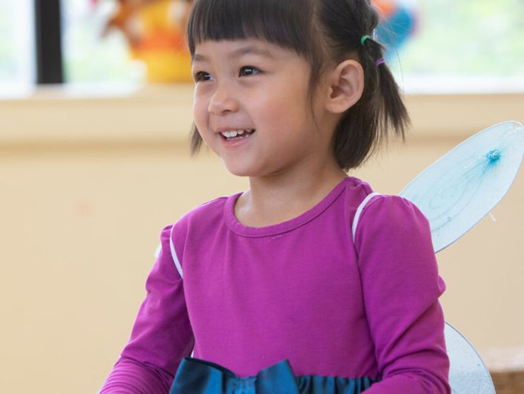 Toddler smiling while wearing fairy wings in classroom at day care 