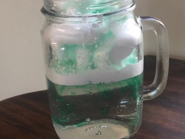 A glass jar with water, shaving cream, and green dye replicating a cloud 