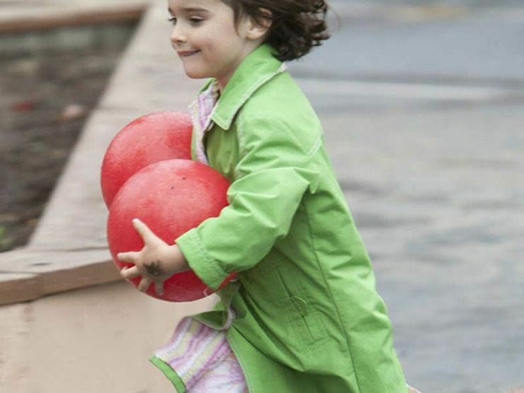 Toddler running around at day care holding two bouncy balls 