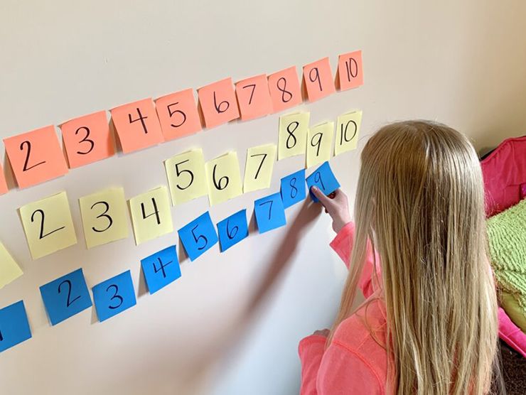 Preschooler learning math with numbered and colored sticky notes on wall at home