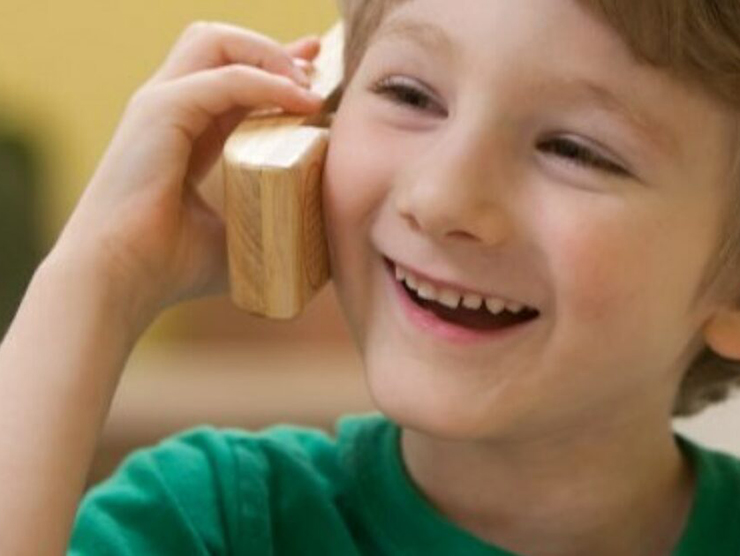 Young boy using a wooden phone and laughing at Bright Horizons day care 