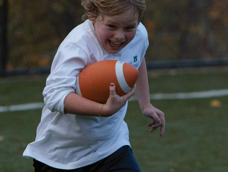 Young boy running across a field with a football in his hand at day care