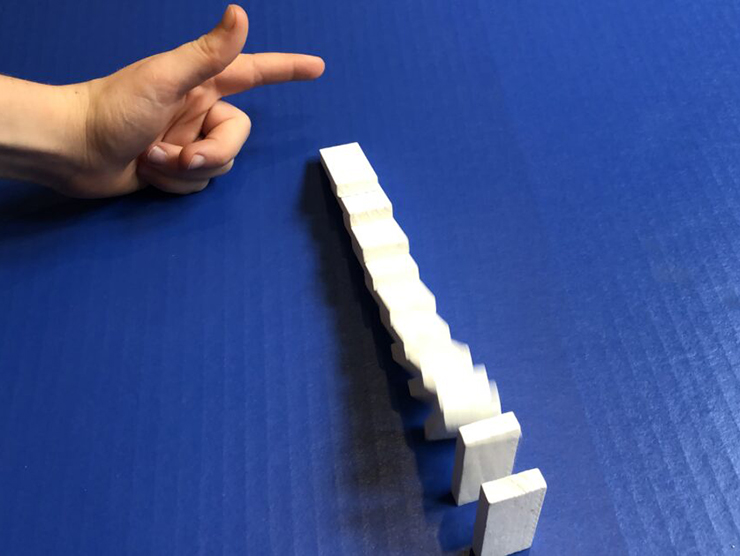 A toddlers hand knocking a row of dominoes over