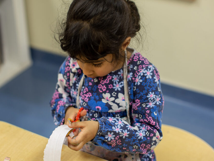 Preschooler using scissors to cut paper for a craft at daycare 