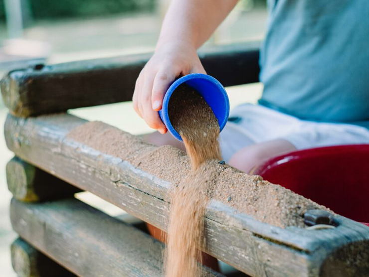 Child developing sensory experience while playing in a sand box outside 