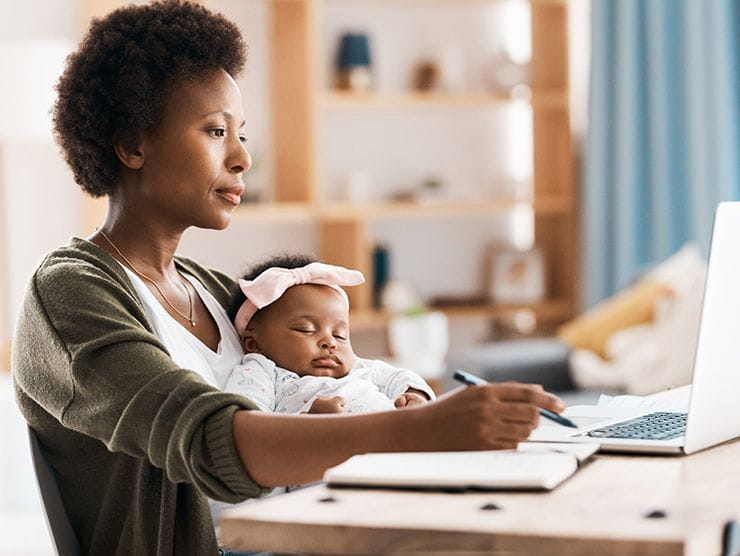 mother at laptop with sleeping baby in arms