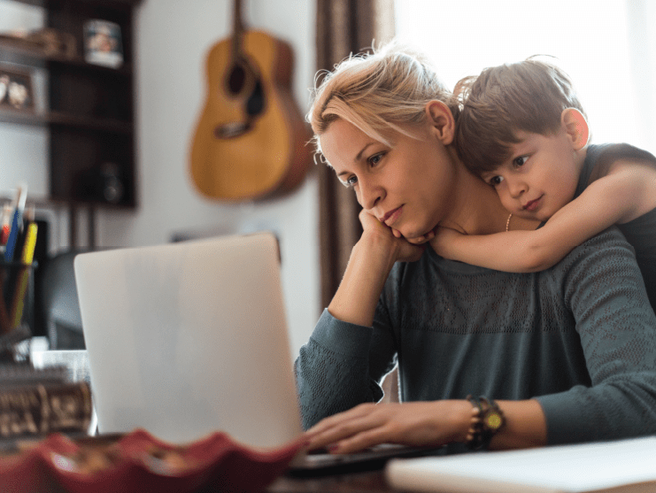 stressed mom on her laptop with son hugging her