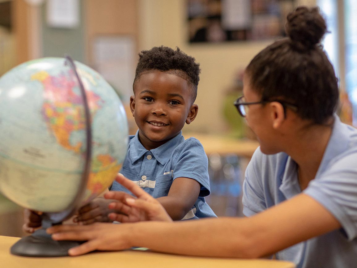 A toddler reviewing a globe with his bright horizons child care teacher.
