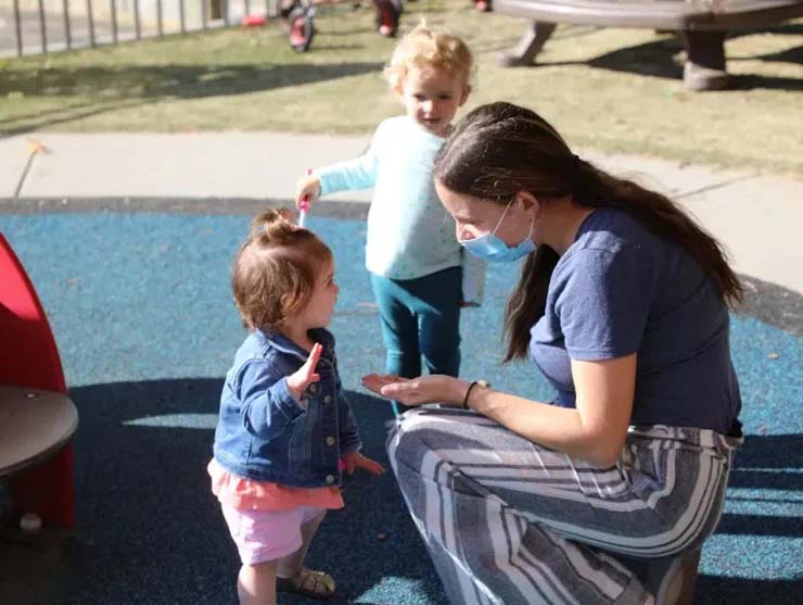 teacher with mask on taking care of children in playground outside