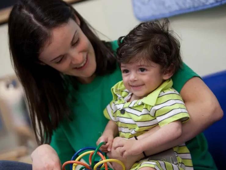 A teacher smiles with a toddler in her arms at daycare