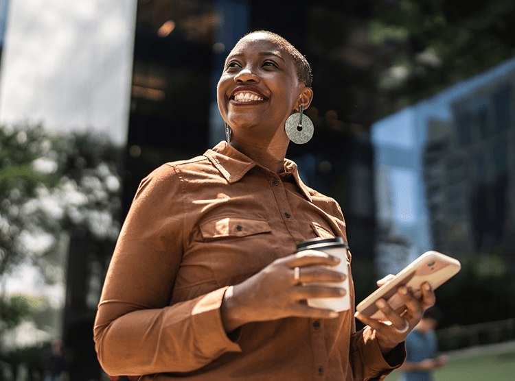 A smiling woman holding her phone and a coffee 