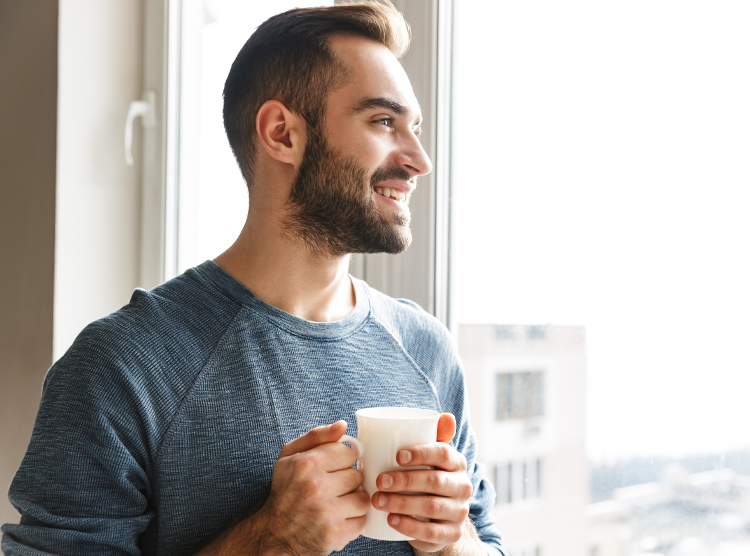 Man smiling while holding a cup of coffee and looking out the window