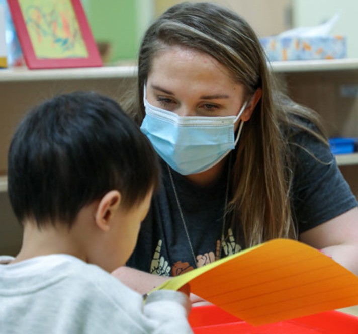 A Bright Horizons teacher helps a young child learn to read while practicing health and safety in a mask