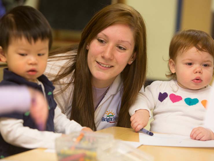 toddler teacher helping two students at Bright Horizons